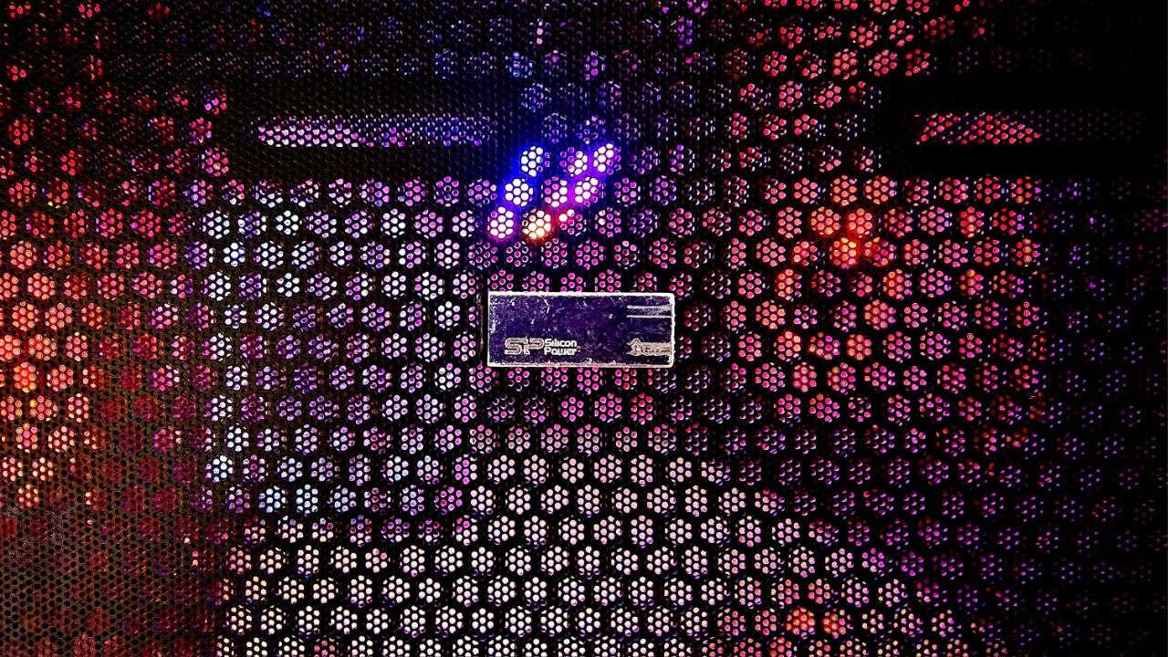 A Silicon Power flash drive resting on the RGB-lit mesh panel of a PC case